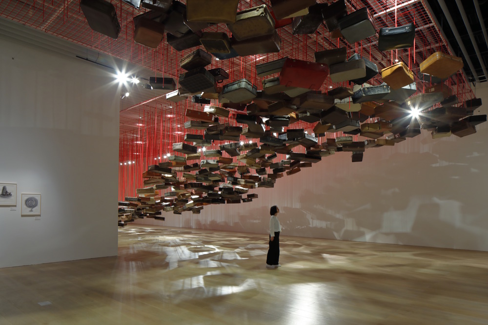 Shiota Chiharu, Accumulation - Searching for the Destination 2014/2019 Suitcase, motor and red rope Dimensions variable Installation view: Shiota Chiharu: The Soul Trembles, Mori Art Museum, Tokyo, 2019 Photo: Kioku Keizo Photo courtesy: Mori Art Museum, Tokyo
